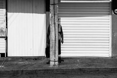 Woman standing behind pole by shop on sunny day