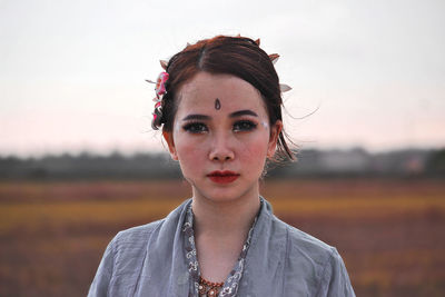 Portrait of young woman standing on field against sky