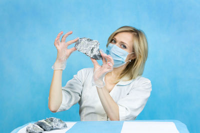 Young woman looking away while sitting against blue background