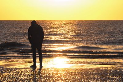 Rear view of silhouette man standing at beach during sunset