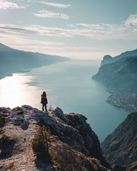 Man standing on rock by sea against sky