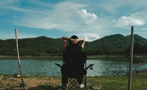 Man sitting by lake against sky