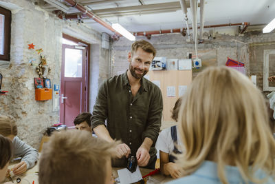 Portrait of smiling male teacher teaching students to work with electrical components at school workshop