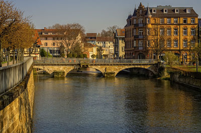 Bridge over river by buildings in city against sky