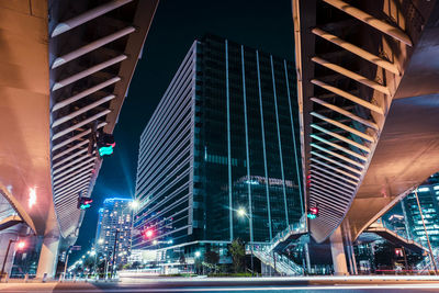 View of the modern pedestrian bridge across the junction leading to the big building at night.