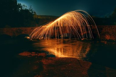 Illuminated ferris wheel by river against sky at night