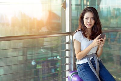 Portrait of young woman using phone while sitting on railing