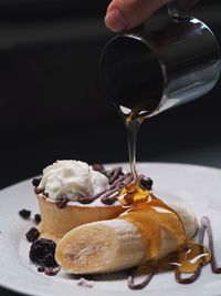 Cropped hand of person pouring sauce on dessert served in plate