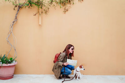 Woman crouching with dog by wall outdoors