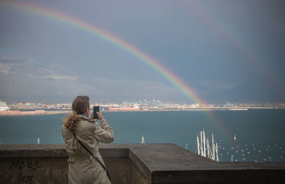 Rear view of woman standing against rainbow in sea
