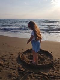 Girl making turtle with sand at beach during sunset