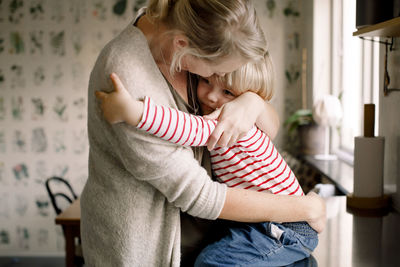 Loving daughter embracing mother while sitting on kitchen counter at home