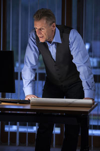 Senior architect or engineer standing at his desk looking at computer screen in a dark office