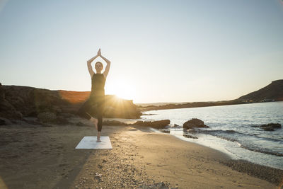 Greece, crete, woman practicing yoga on the beach at sunset