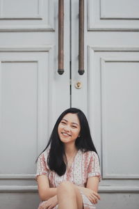 Portrait of smiling young woman sitting against door