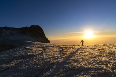 Person on snowcapped mountain against sky during sunset