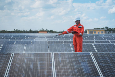 Engineer standing amidst solar panel against cloudy sky