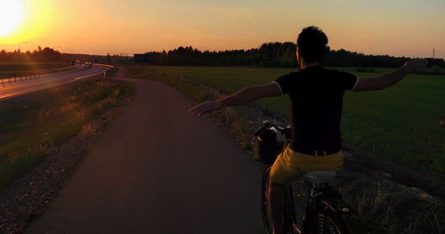 Rear view of man with bicycle against sky during sunset