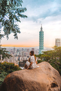 Woman sitting by buildings against sky