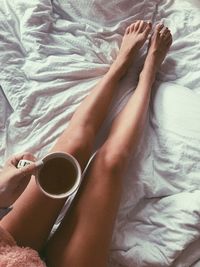 Low section of woman having coffee on bed