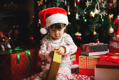 Cute girl opening christmas present against tree at home