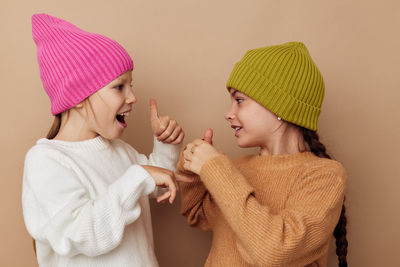 Sibling wearing knit hat gesturing against beige background