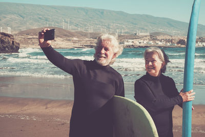 Smiling senior man with woman taking selfie from mobile phone at beach on sunny day