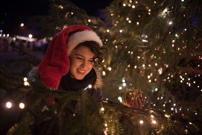 Happy young woman with gift by illuminated christmas tree at night