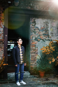 Young man looking away while standing against wall
