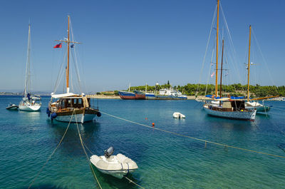Sailboats moored in sea against clear blue sky