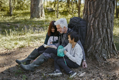 Full length of friends sitting on tree trunk