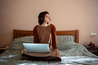 Tired teen girl sitting on bed, having break after long freelance work, hard online studying
