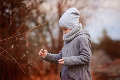 Side view of boy standing near the willow tree and touching the twig 