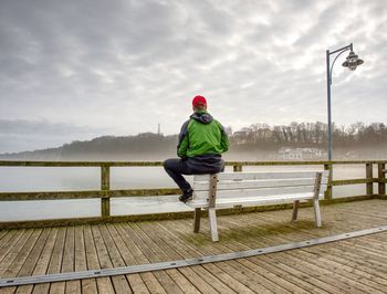 Rear view of man standing by railing against smooth baltic sea during rainy season