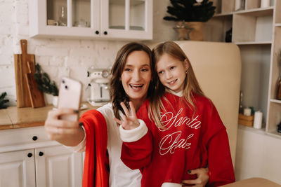 Mom and daughter in red sweaters take selfies using mobile phone and technology on holiday