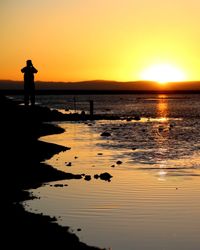 Silhouette man standing at beach against sky during sunset