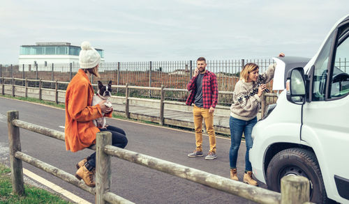 Woman repairing car while man talking on phone on road