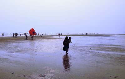 People walking on beach against clear sky