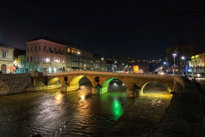 Illuminated bridge over river against sky in city at night