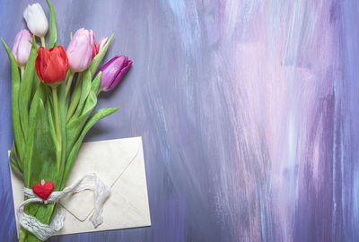 Close-up of tulips and envelop hanging on blackboard