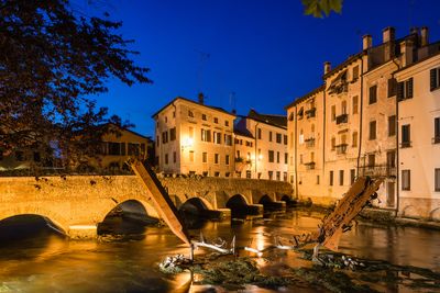 Arch bridge over river by illuminated building at night