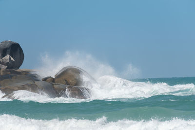 Waves splashing on rocks against sky