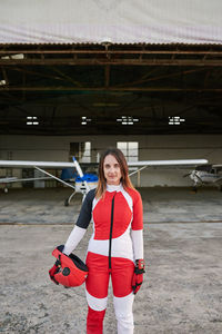 Young female skydiver in a hangar with a plane behind her