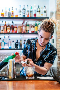 Focused male bartender with dreadlocks pouring alcohol in glass and preparing delicious cocktail at counter in bar