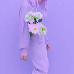 Midsection of woman with pink flowers against colored background