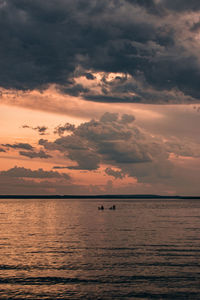 People sailing in sea against sky during sunset