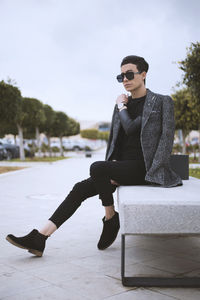 Full length of male model sitting on bench in city