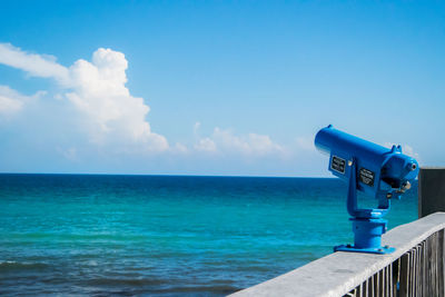 Blue coin-operated binoculars at observation point by sea against sky