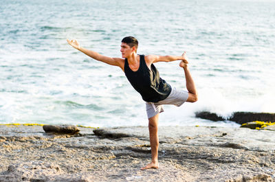 Full length of man doing yoga at beach