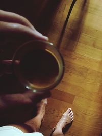 Midsection of person holding cup on hardwood floor